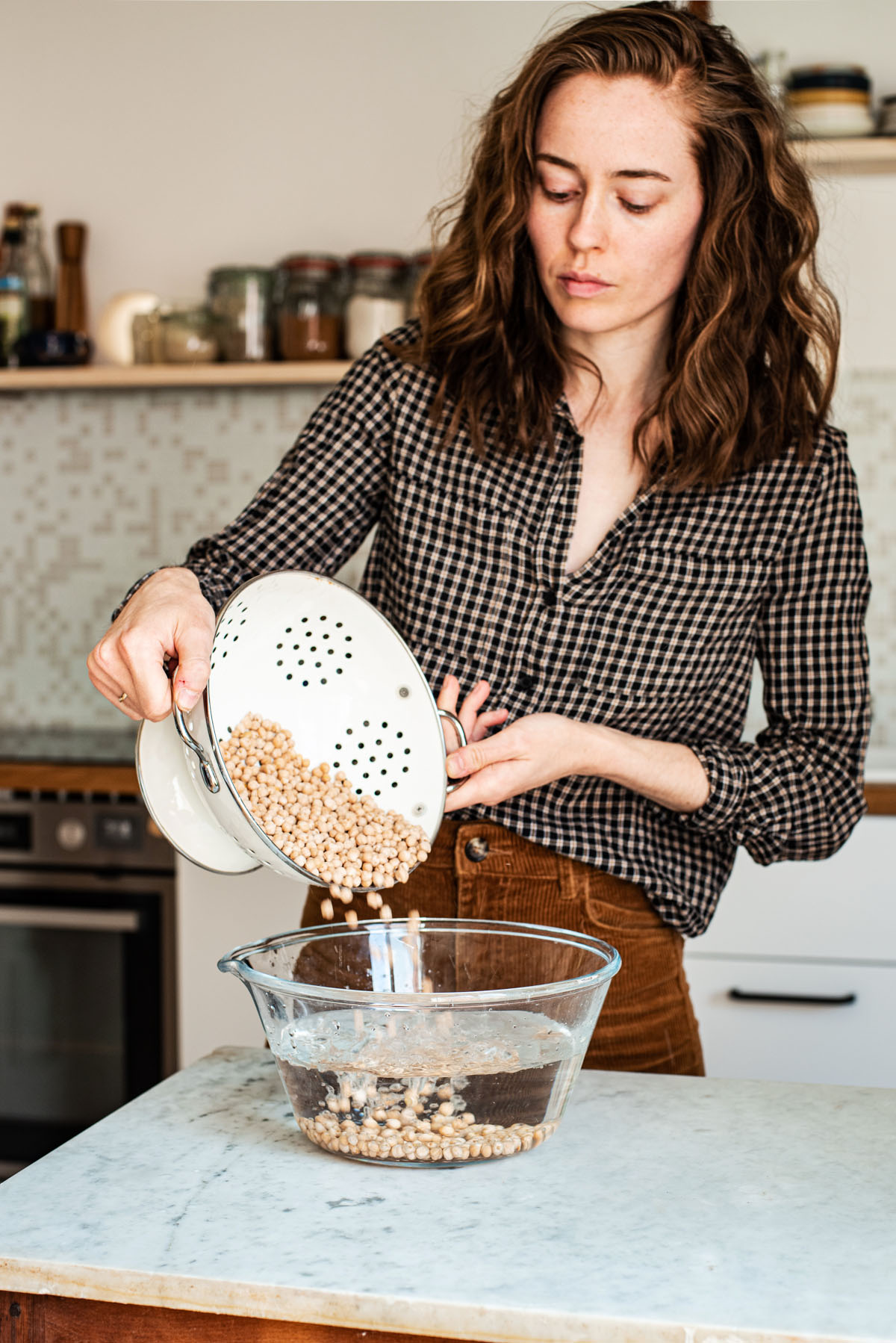 Woman pouring chickpeas into a bowl of water.